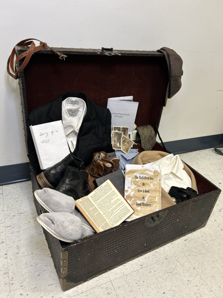 a replica trunk containing boy's clothes, books, and photographs